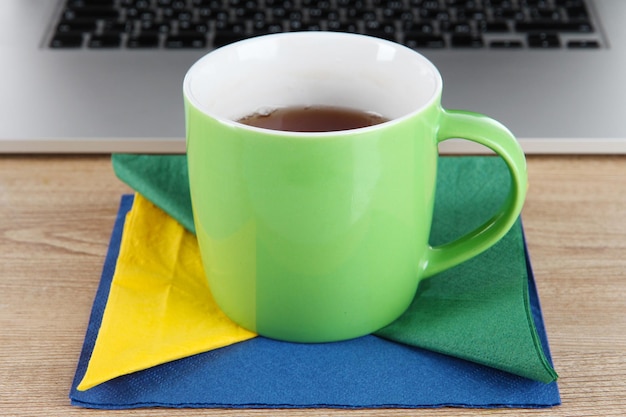 Grüne Tasse auf Serviette auf Laptophintergrund auf Holztisch