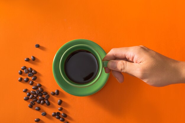 Grüne Tasse Kaffee mit Kaffeebohnen auf orange Hintergrund nehmen