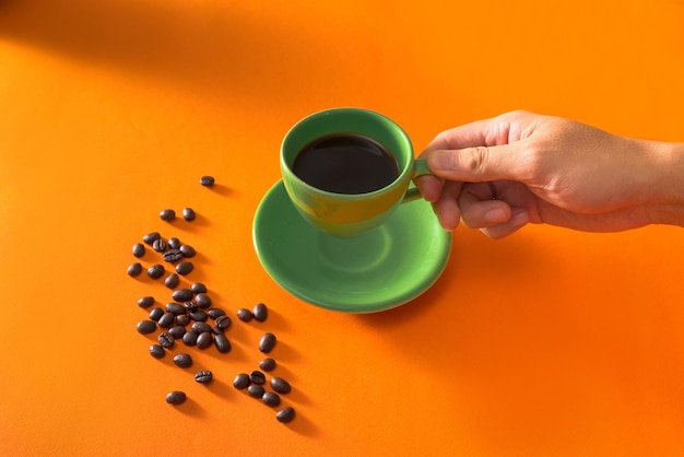 Grüne Tasse Kaffee mit Kaffeebohnen auf orangem Hintergrund nehmen