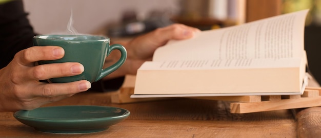 Grüne Tasse mit heißem Kaffee in den Händen der Frau mit Lesebuch zu Hause konzentrieren sich auf die Tasse