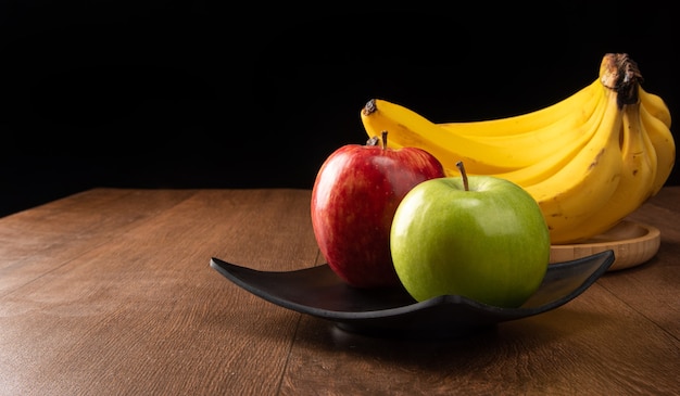 Grüne und rote Äpfel auf schwarzem Teller und Bananen auf Holz