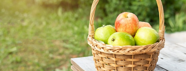 Grüne und rote Äpfel im Weidenkorb auf Holztisch Grünes Gras im Garten Erntezeit Horisontal Banner