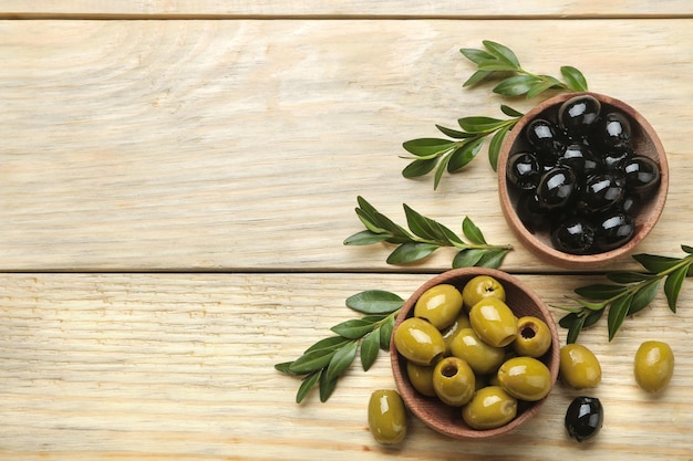 Grüne und schwarze Oliven in einer Holzschale mit Blättern auf einem Naturholztisch. Ansicht von oben. Platz für Text