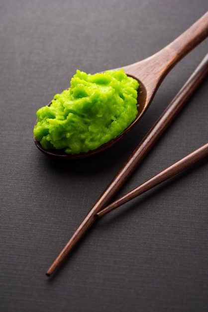 Foto grüne wasabi-sauce oder paste in schüssel, mit stäbchen oder löffel über einfarbigem, buntem hintergrund. selektiver fokus