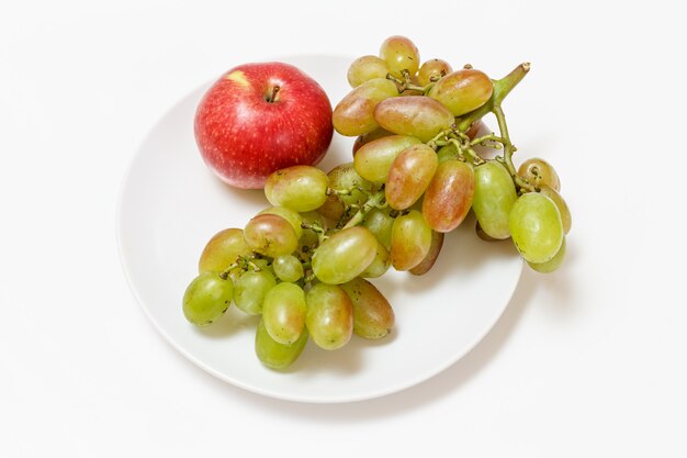 Grüne weintrauben und ein apfel auf einem teller mit weißem hintergrund. ansicht von oben.