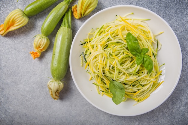 Grüne Zoodles oder Zucchinispaghetti auf Teller über grau