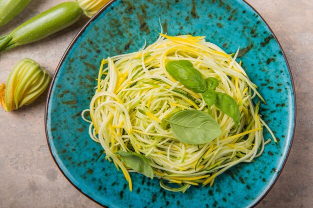 Grüne Zoodles oder Zucchinispaghetti auf Teller über grau