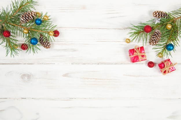 Grüne Zweige eines Weihnachtsbaumes, verziert mit Zapfen und bunten glänzenden Kugeln auf einem weißen Holz