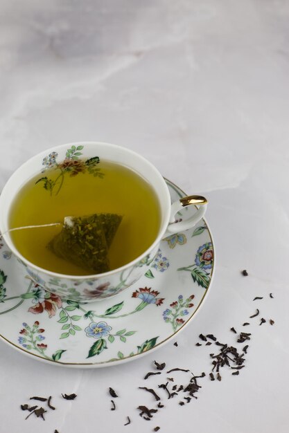 Grünen Tee in einer Tüte in einer Porzellantasse in einer Untertasse mit Blumenbild aufbrühen