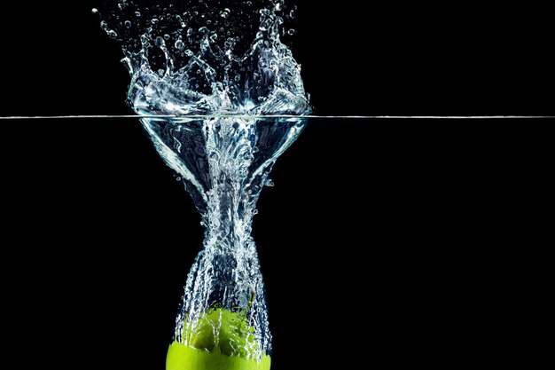 Grüner Apfel, der in Wasser mit einem Spritzer gegen dunkle Wandnahaufnahme fällt