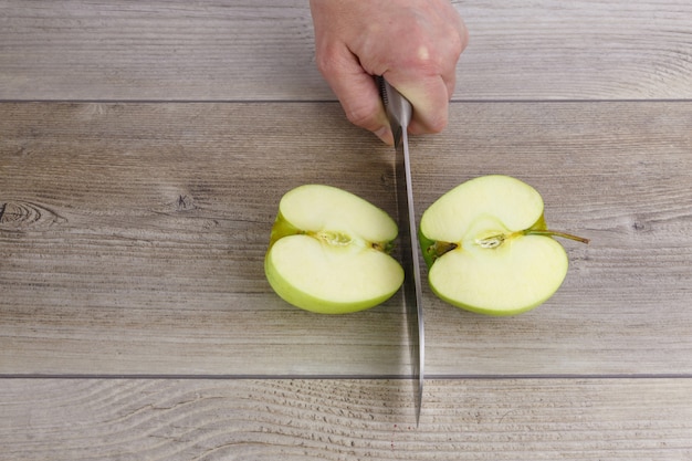 Foto grüner apfel, der von einem messer auf einem holztisch geschnitten wird