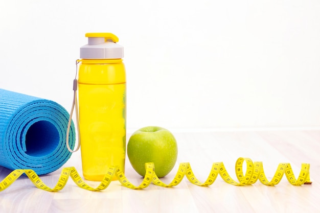 Grüner Apfel, Maßband, Wasserflasche und Sportmatten auf einem hellen hölzernen Hintergrund. Gewichtsverlust und Sportkonzept