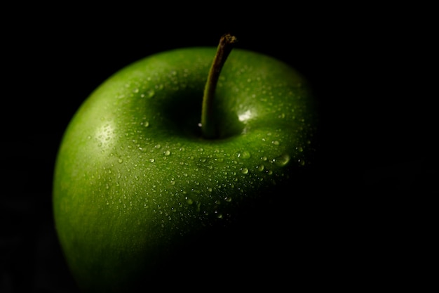 Grüner Apfel mit Tropfen auf dunkler Wand