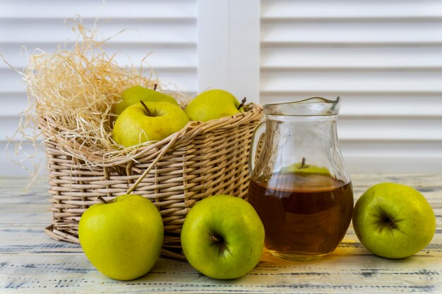 Grüner Apfelkorb mit Äpfeln und Krug mit Apfelsaft auf hölzernem Hintergrund