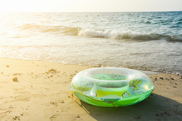 Grüner aufblasbarer runder Rohr- oder Plastikschwimmring auf dem Sandstrand mit Sonnenlicht am Abend