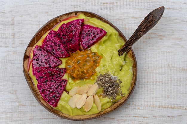 Grüner Avocado-Smoothie in Kokosnussschale mit Drachenfrucht-Passionsfrucht-Mandelflocken, Kokoschips und Chiasamen zum Frühstück aus nächster Nähe Das Konzept der gesunden Ernährung Superfood