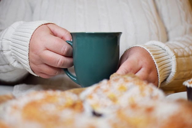 Grüner Becher mit Tee oder Kaffee in den Händen der Frau. Frühstückszeit oder Kaffee- oder Teepause.