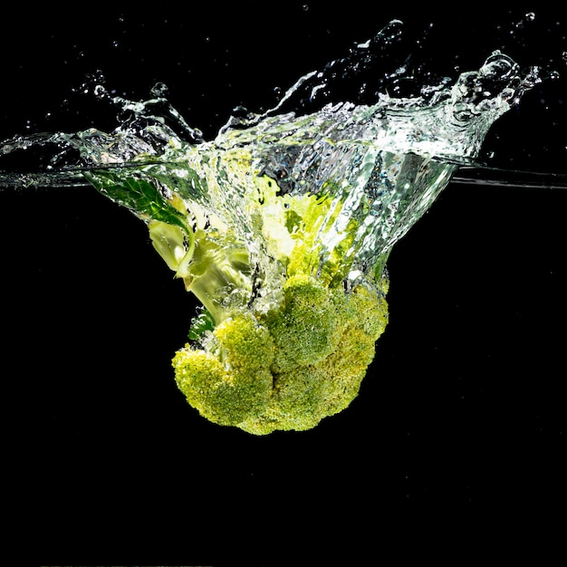 Foto grüner brokkoli spritzt in sauberes wasser über dem schwarzen hintergrund