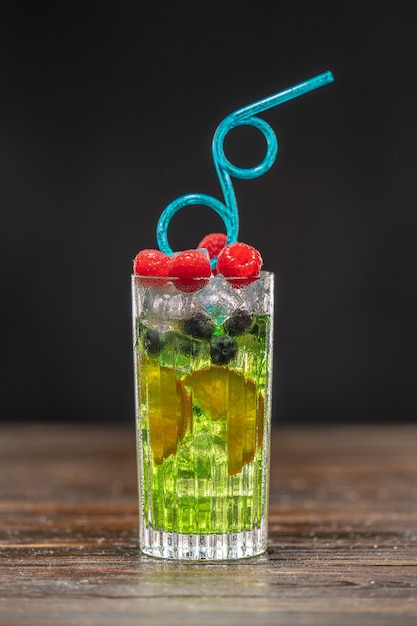 Foto grüner cocktail in einem hohen glas, dekoriert mit orange, himbeeren und blaubeeren