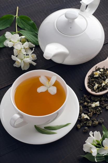 Grüner duftender Tee mit Jasmin in Tasse und Teekanne auf dunklem Holzhintergrund. Ansicht von oben.