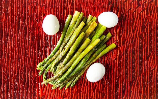 Foto grüner gegrillter spargel und gebackene eier auf einer roten quadratischen glasplatte