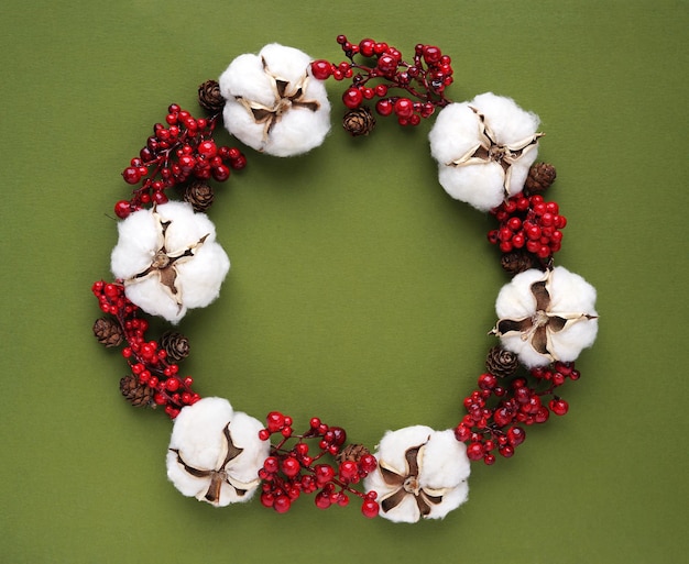 Grüner Hintergrund mit einem Weihnachtskranz aus roten Beeren und Blumen aus Baumwolle