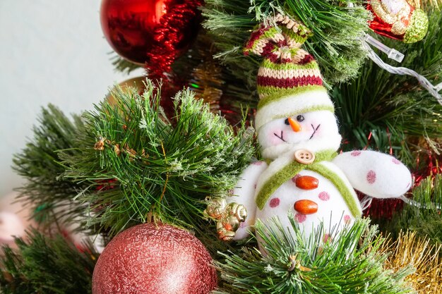 Grüner künstlicher Weihnachtsbaum verziert mit schönem lächelndem Textilschneemann, roten Kugeln und anderem Spielzeug. Heimtextilien für einen Familienurlaub. Selektiver Fokus