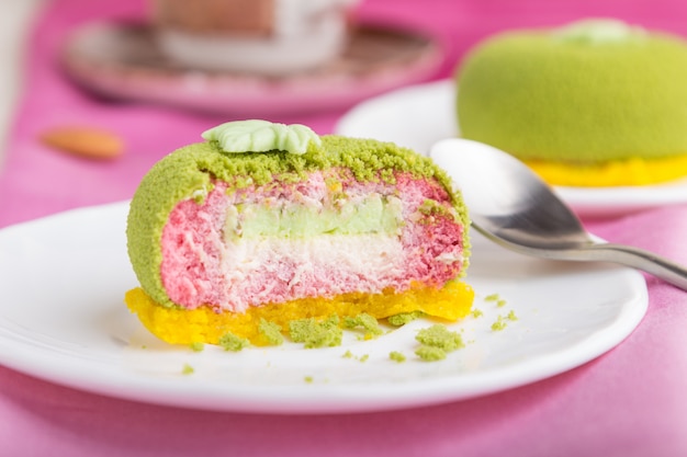 Grüner Moussekuchen mit Pistazien- und Erdbeercreme auf einem rosa Textilhintergrund. Seitenansicht, selektiver Fokus.