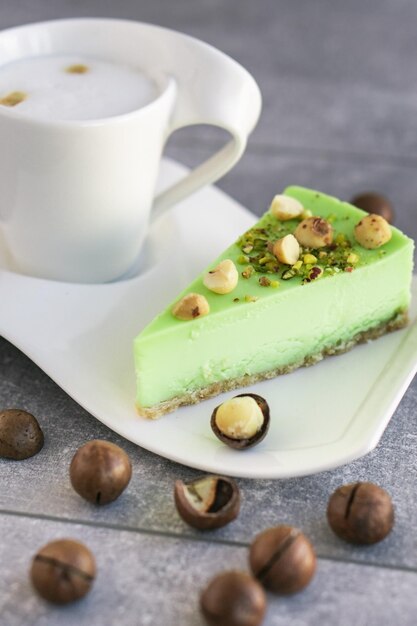 Grüner Pistazienkuchen mit Macadamianüssen auf weißem Teller mit Cappuccino Cremiger Pistazien-Käsekuchen