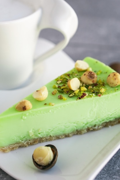 Grüner Pistazienkuchen mit Macadamianüssen auf weißem Teller mit Cappuccino Cremiger Pistazien-Käsekuchen