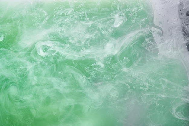 Grüner Rauch auf weißem Tintenhintergrund, bunter Nebel, abstrakter, wirbelnder Smaragdozean, Acrylfarbe, Pigment unter Wasser