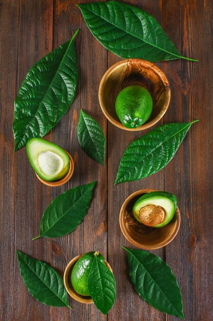 Grüner roher reifer Schnitt und ganze Avocadofrüchte mit Stein liegen in hölzernen Schüsseln