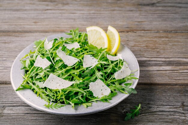 Grüner Rucola-Salat mit Parmesan-Käse-Zitronen-Olivenöl und Gewürzen auf Holzhintergrund