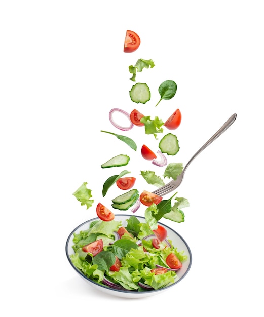 Grüner salat, der auf einem weißen hintergrund in einen teller fällt