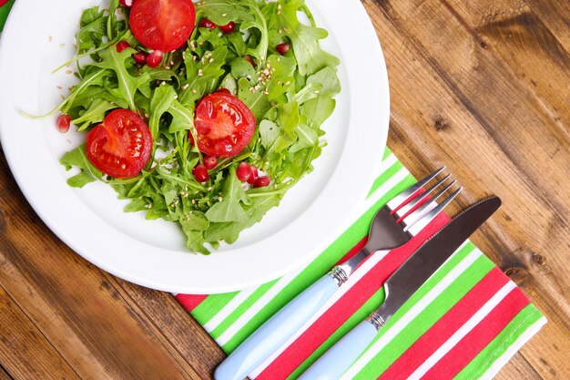 Grüner Salat mit Arugula-Tomaten und Sesam auf Teller auf Holzhintergrund