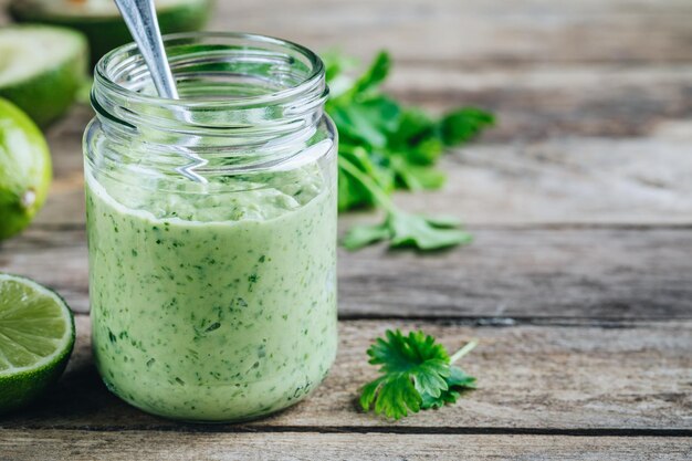 Grüner Salatdressing mit Avocado-Limette und Koriander in einem Glasgefäß auf rustikalem Hintergrund