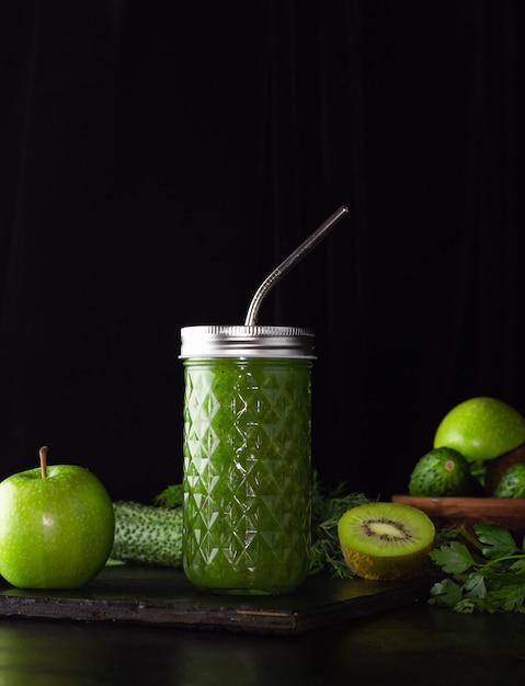 Grüner Smoothie in einem Glasglas auf schwarzem Hintergrund. Kiwi, Äpfel, Gurken und Grüns. Gesundes Essen kochen. Null weist ein Metallrohr auf.