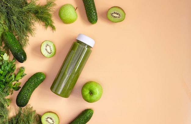 Grüner Smoothie in einer transparenten Flasche auf beigem Hintergrund. Das geschnittene Obst und Gemüse wird ausgelegt. Gesundes Essen, flach. Exemplar.