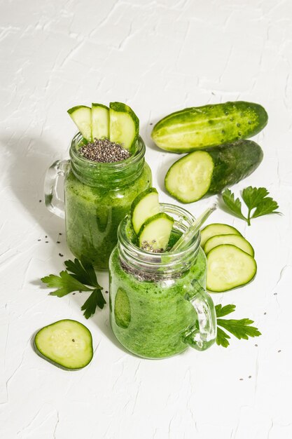 Grüner Smoothie mit Gurke in einem Glasgefäß. Frisches reifes Gemüse, Gemüse und Chiasamen. Trendiges hartes Licht, dunkler Schatten. Weißer Kitthintergrund, Nahaufnahme