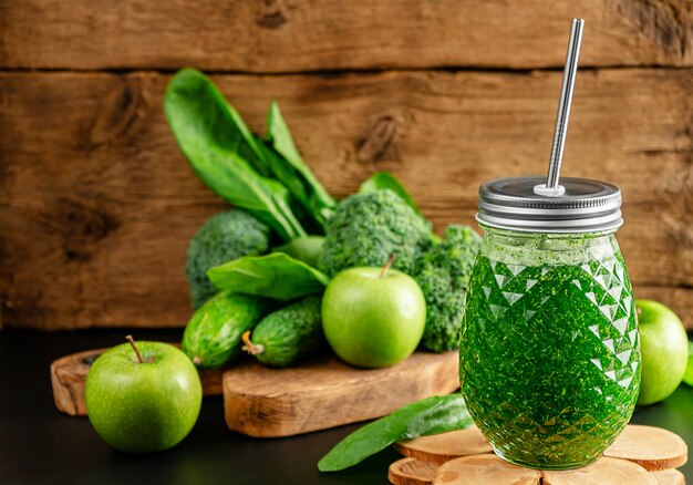 Grüner Smoothie mit Zutaten auf Holzwand.