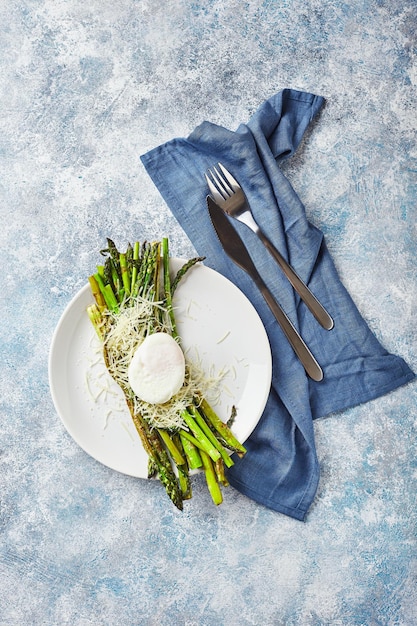 Grüner Spargel mit pochiertem Ei und vegetarisches Frühstück mit Parmesan, serviert auf weißem Teller auf hellem Hintergrund