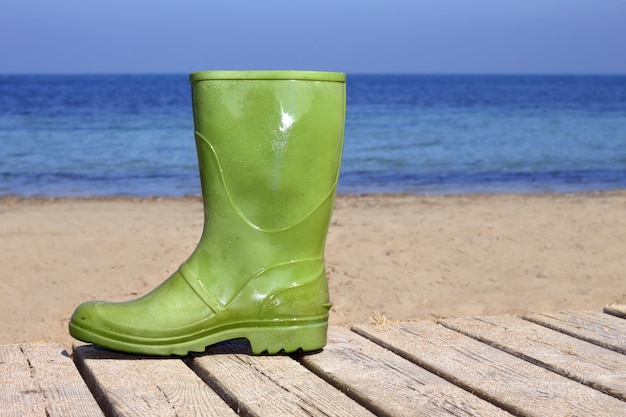 Grüner Stiefel auf unglücklicher Fischermetapher des Strandes