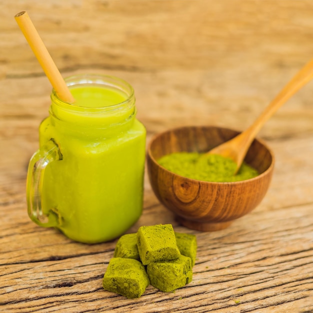 Grüner Tee Latte mit Eis im Einmachglas Matcha-Pulver und Süßigkeiten aus Matcha auf Holzhintergrund