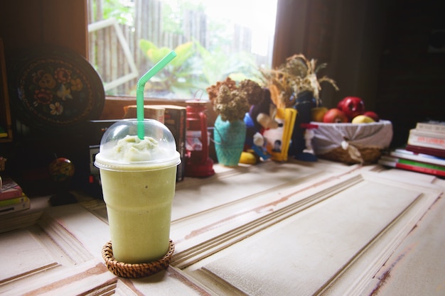 Grüner Tee Milch Frappe in klarem Plastikglas haben grünes Stroh auf hölzernem Regal.