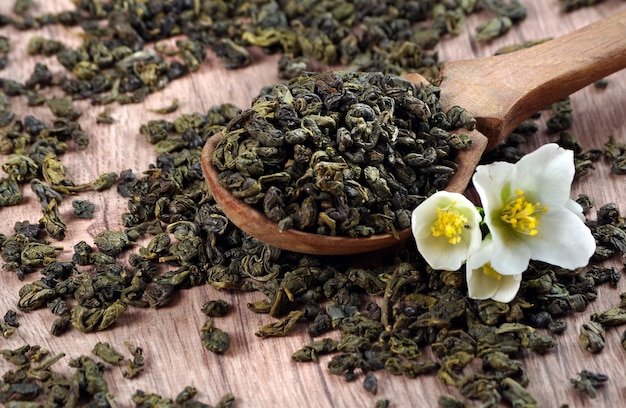 grüner Tee mit Jasmin. grüne Teeblätter in einem Holzlöffel und Jasminblüten.
