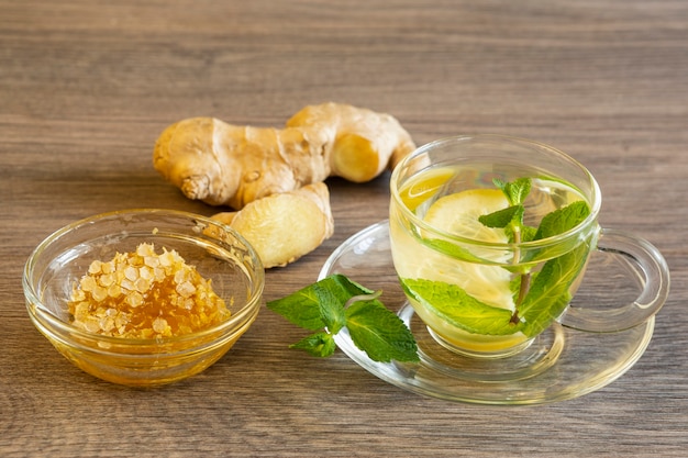 Grüner Tee mit Zitrone und Minze, Ingwer und Honig in einer Glasschüssel auf einem Holztisch