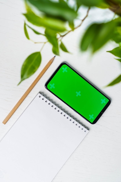 Grüner Urlaub mit leerem Notizblock Smartphone Green Screen Mockup und Bleistift flach liegen Draufsicht