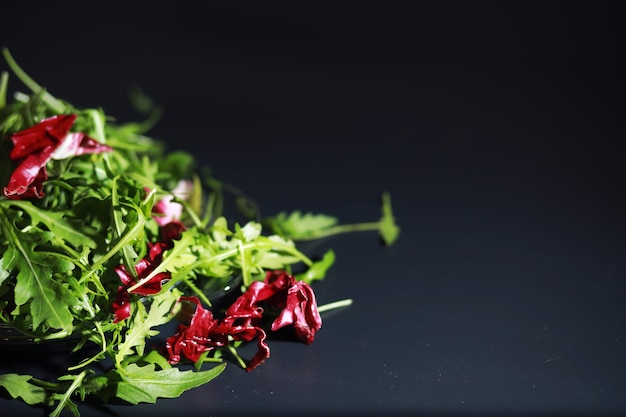 Grüner veganer Salat aus grünem Blättermix und Gemüse. Frische Rucolablätter in einem Sieb. Schwarzer Hintergrund.