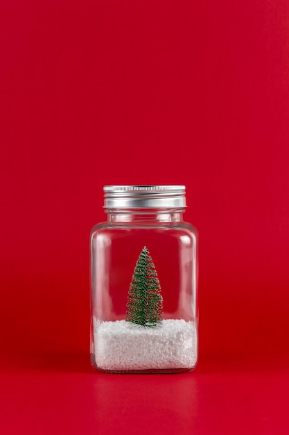 Grüner Weihnachtsbaum mit Schnee in einem Glas auf rotem Grund