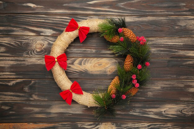 Grüner Weihnachtskranz verziert mit roter Schleife auf braunem hölzernem Hintergrund. Erntedank. Draufsicht.